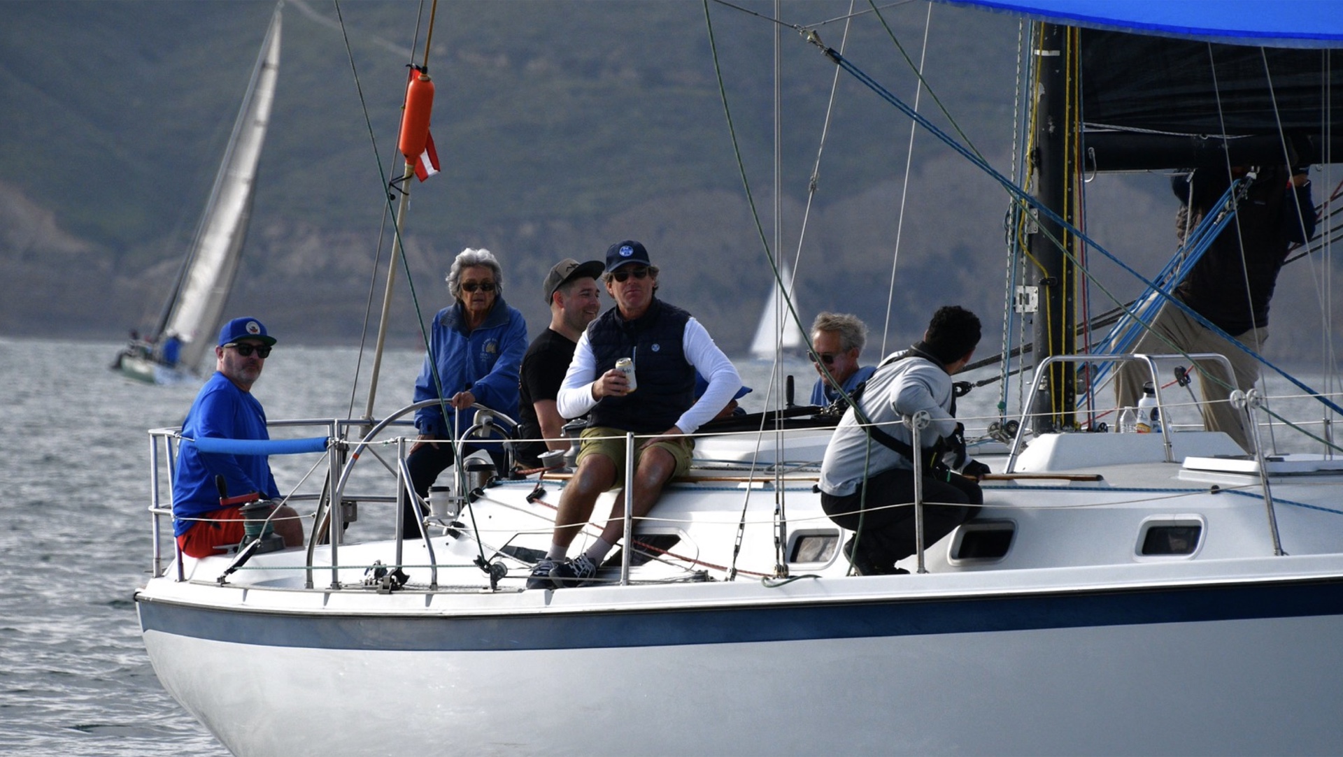 Sailboat crew enjoying Corinthian camaraderie on deck under sail in coastal waters